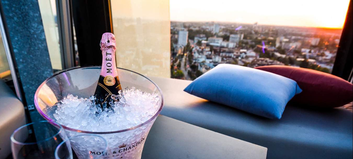 Champagner im Kühler auf einem Tisch vor Sitzbank mit Kissen und Sonnenuntergang